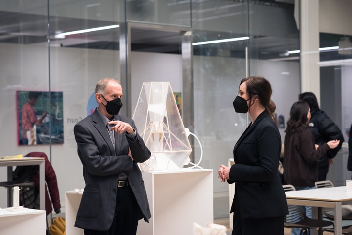 Two people stand and chat in front of several abstract architectural models.
