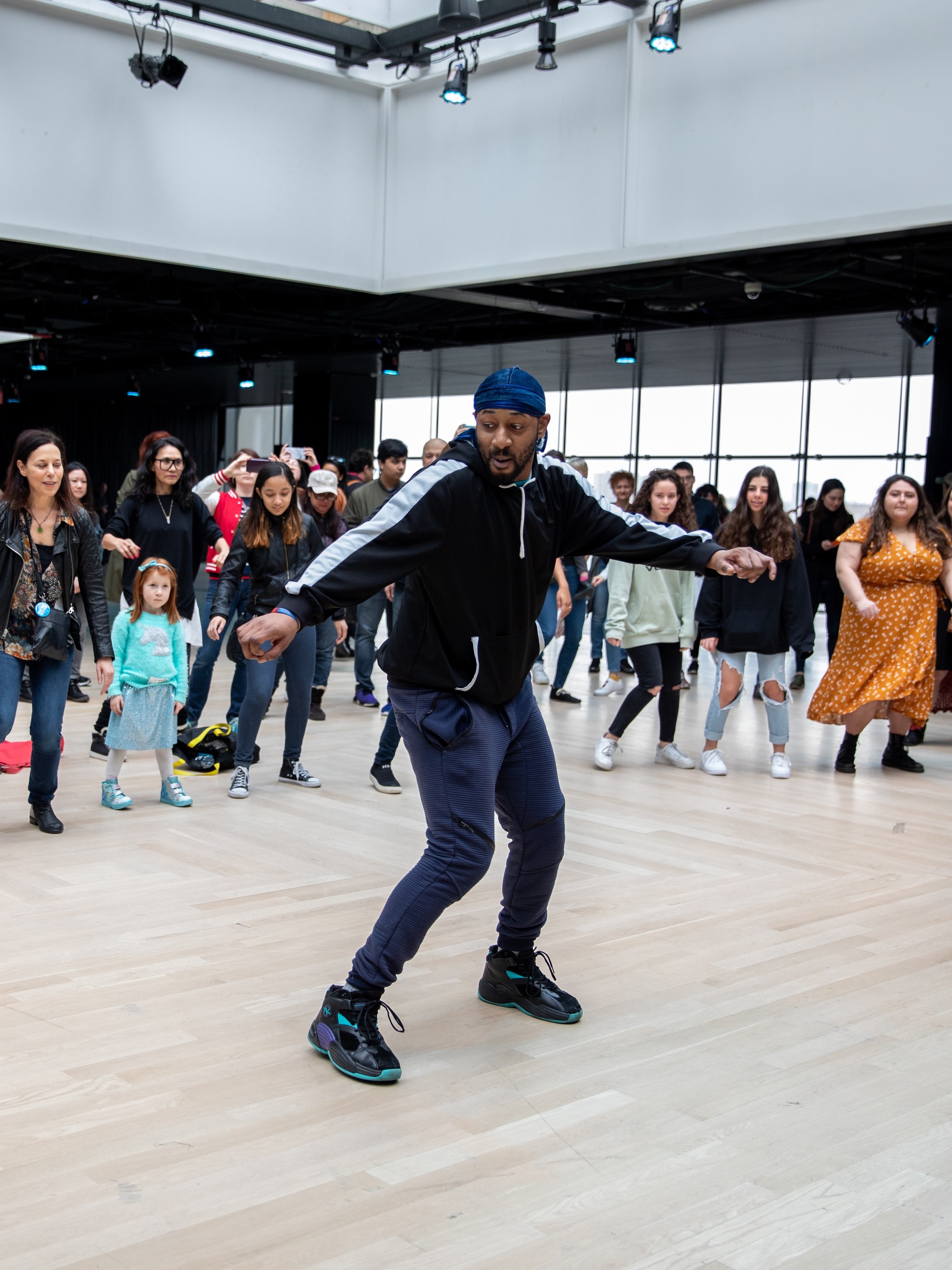 A man leading a dance workshop with participants behind him in a line in a well lit event space