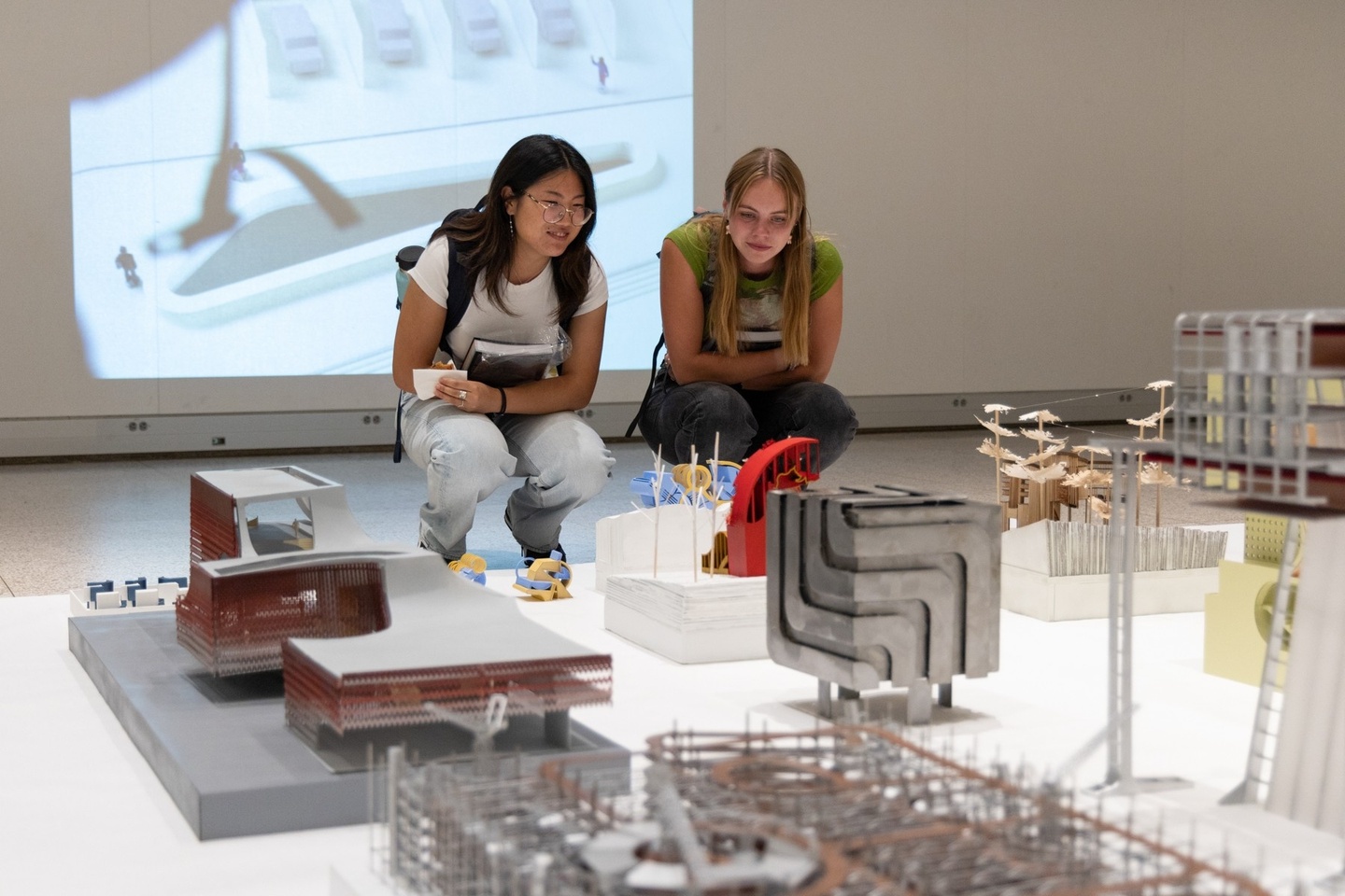 Two people crouching looking at architectural models that are displayed on the floor.