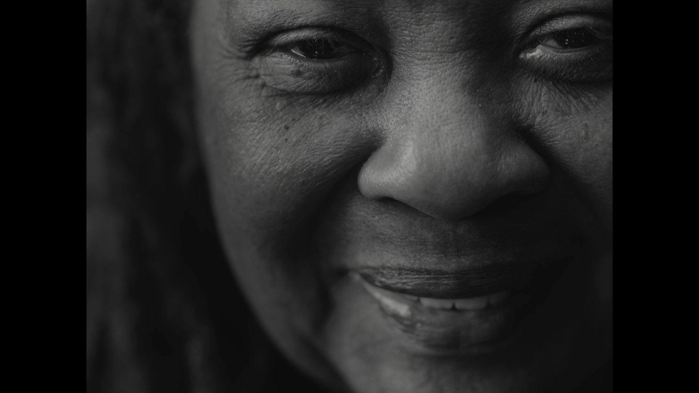 A black-and-white image up close of a smiling dark-skinned woman