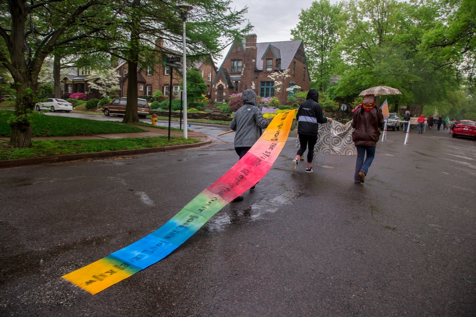 People walking on a road in some kind of protest. A long banner trails behind a person depicting the text 'How high does the sycamore grow, if you cut it down then you'll never know'