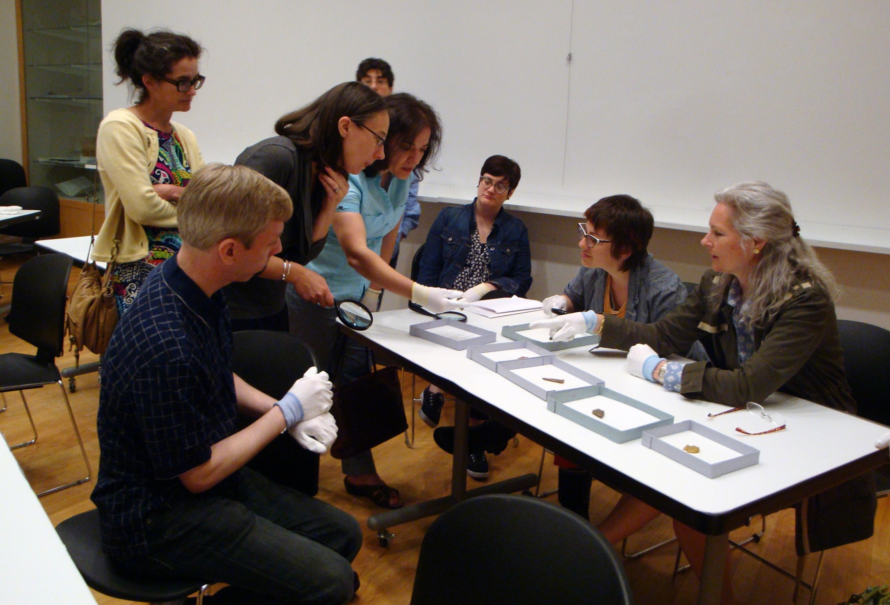 A group of people look at objects on a table top.