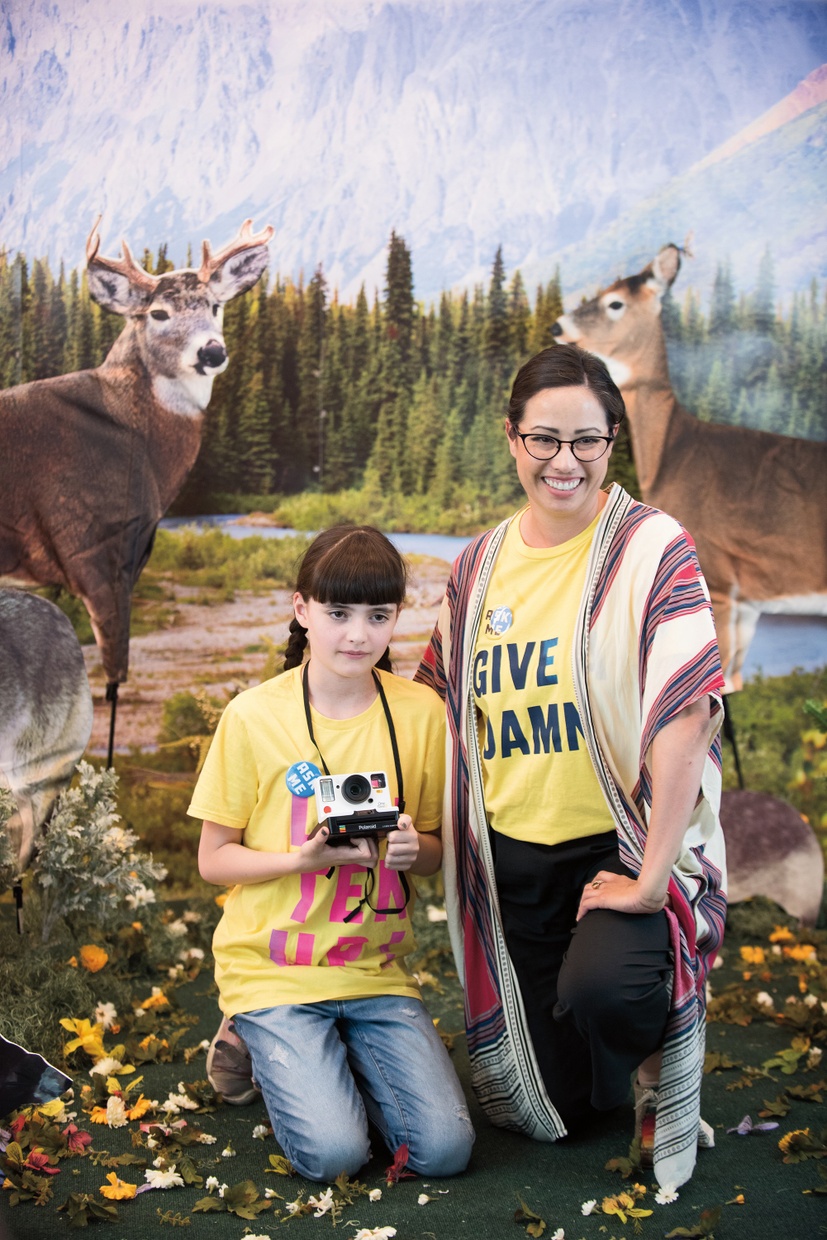A girl kneels smiling next to her motherin front of a fake naturescape.