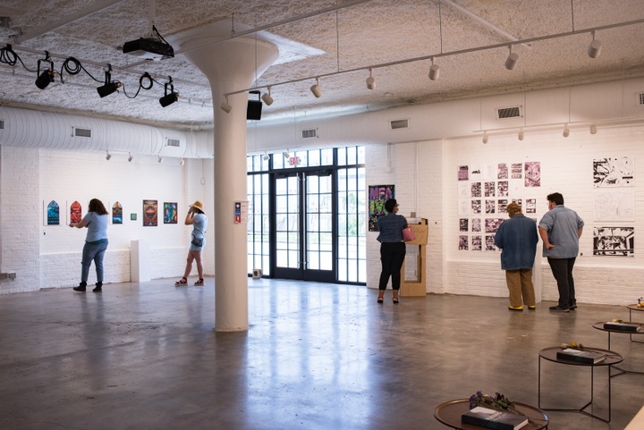 Wide shot of gallery space with several visitors looking at art prints and comics pages on the walls.