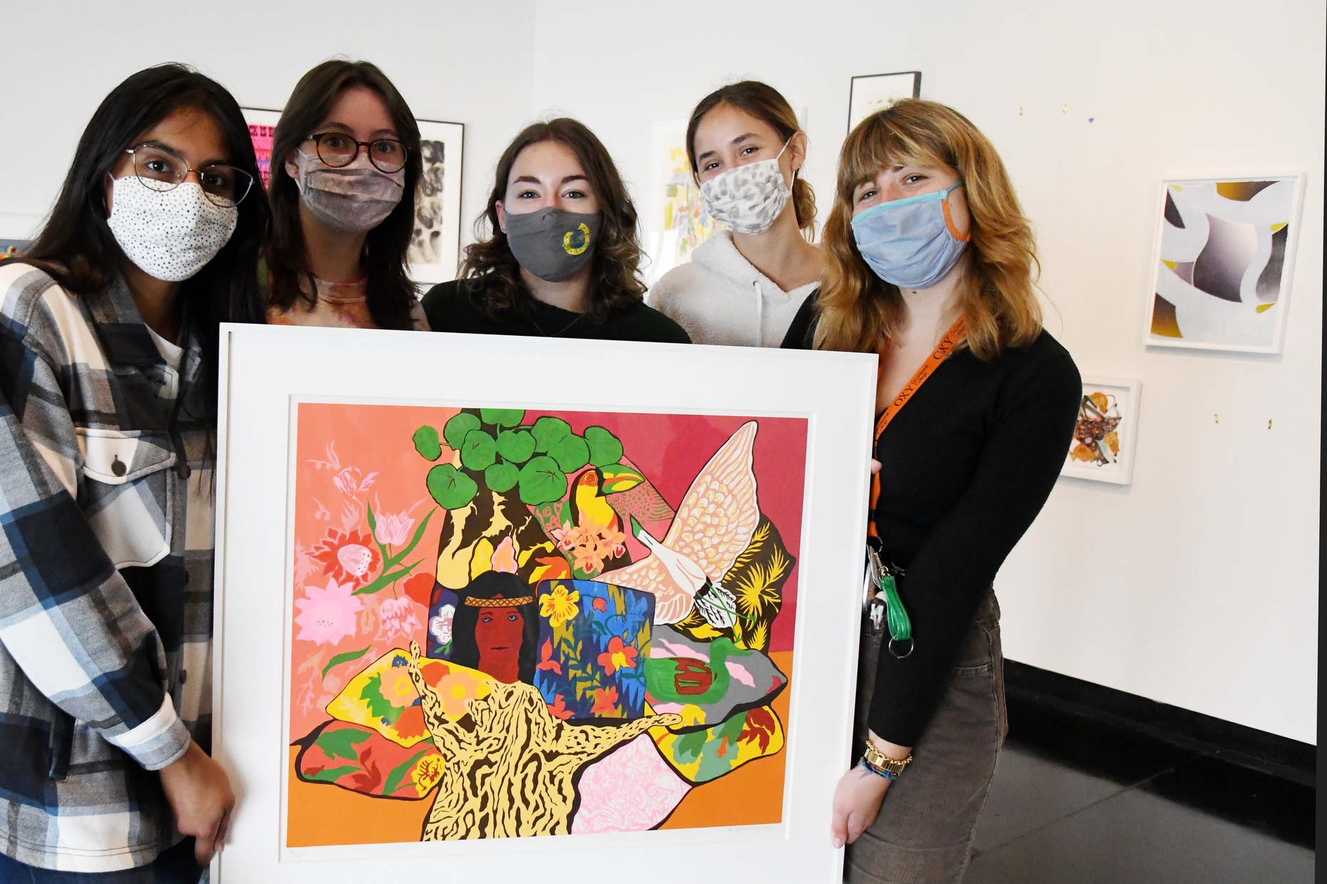 Five masked students stand in a group looking at the camera holding one large framed print by artist Hunt Slonem.