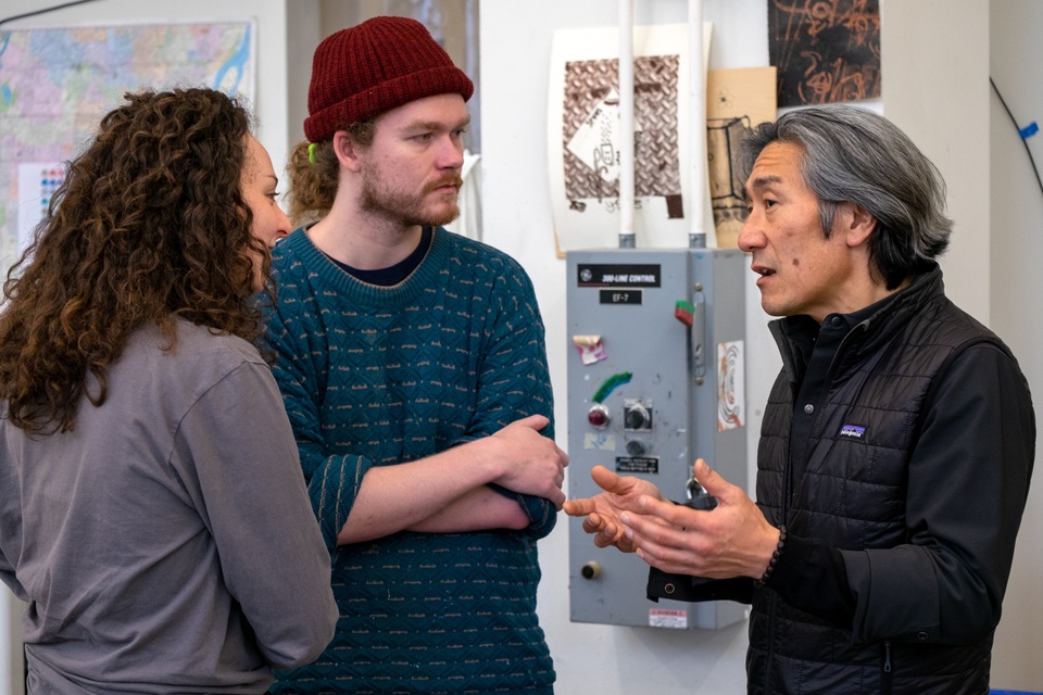 Two people listen attentively to a third person talking and gesturing.