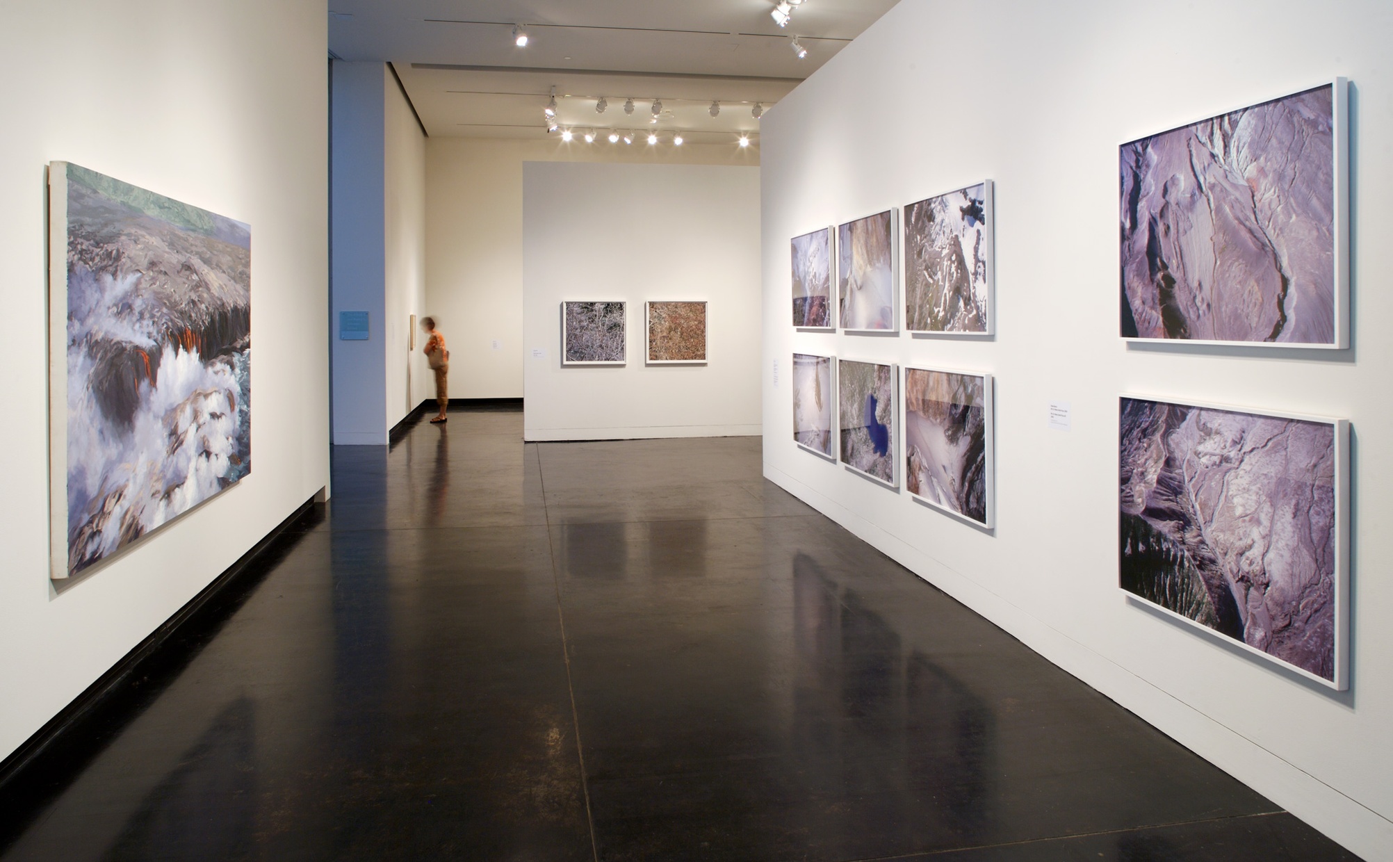 Framed photographs of geographic scenes hang on white walls in a gallery space.