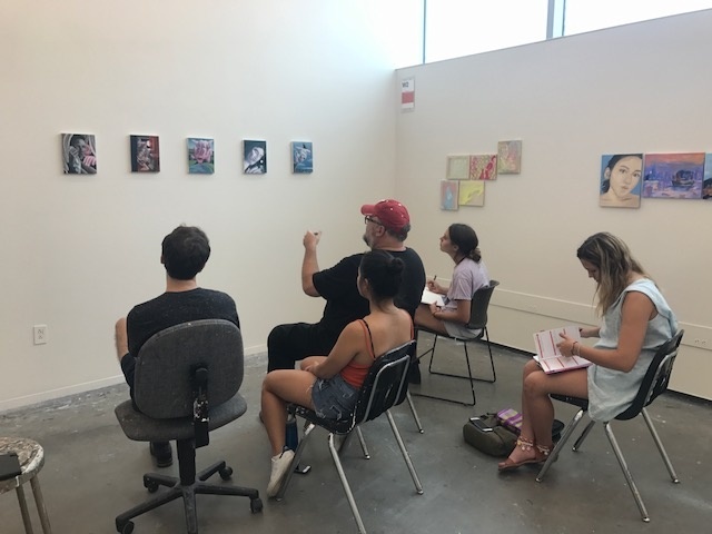 Jamie Adams sits in front of class critiquing a students work on display