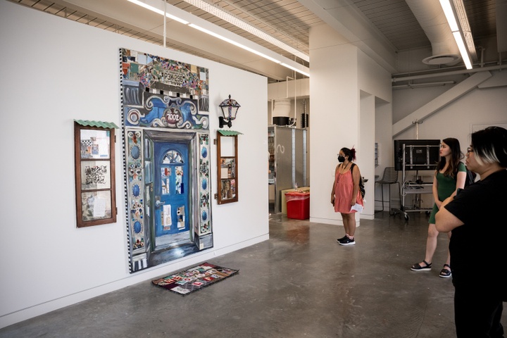 Gallery view of a large painting of an ornate blue door flanked by brown windows on each side