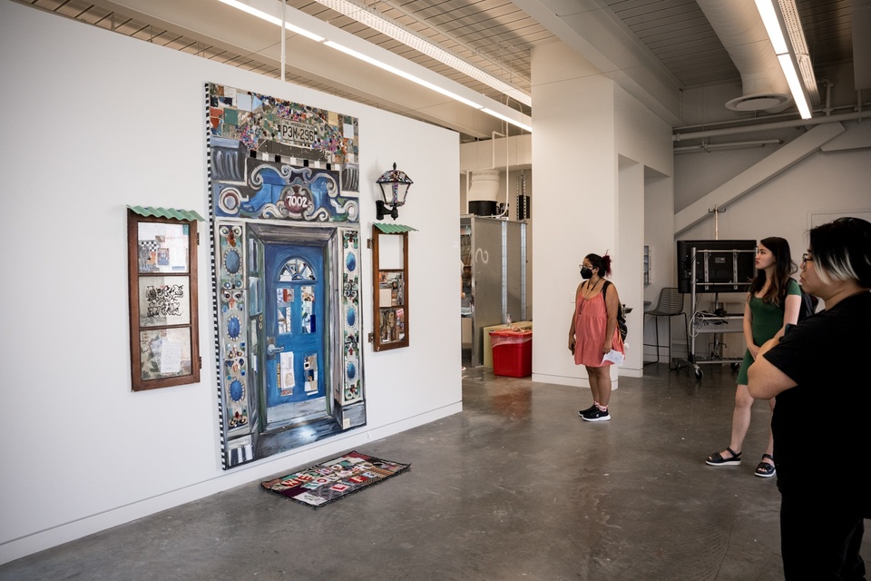 Gallery view of a large painting of an ornate blue door flanked by brown windows on each side