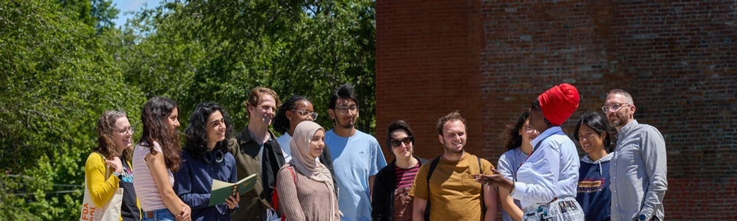 A group of WashU Sam Fox School students outdoors listening to a community member as part of the Summer Public Design Workshop