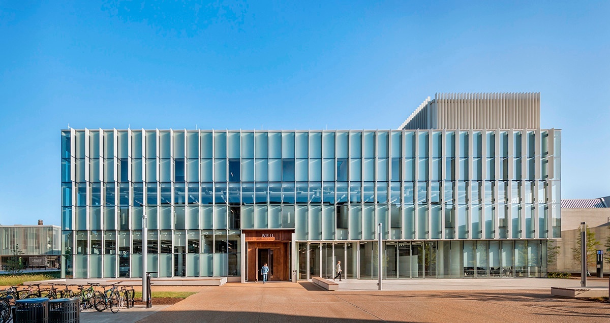 Exterior facade of three-story contemporary building with pleated fins and a large wooden door on the ground level.