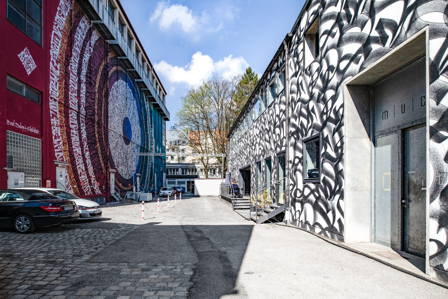 Alleyway between two industrial-looking buildings with bold, graphic mural painting on the exterior.