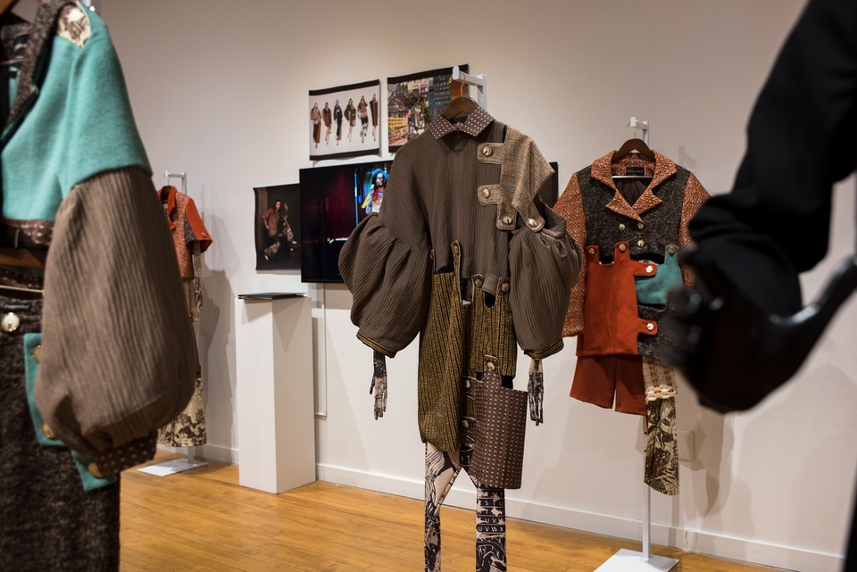 View of a short dress with baloon sleeves constructed from heavy brown and beige fabrics patchworked together with tabs and buttons.