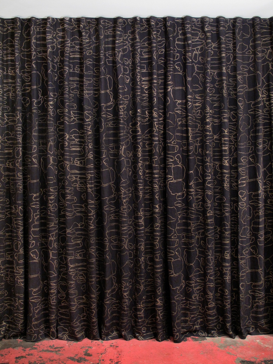 a floor length dark blue curtain with a gold geometric line pattern hangs with a red floor below