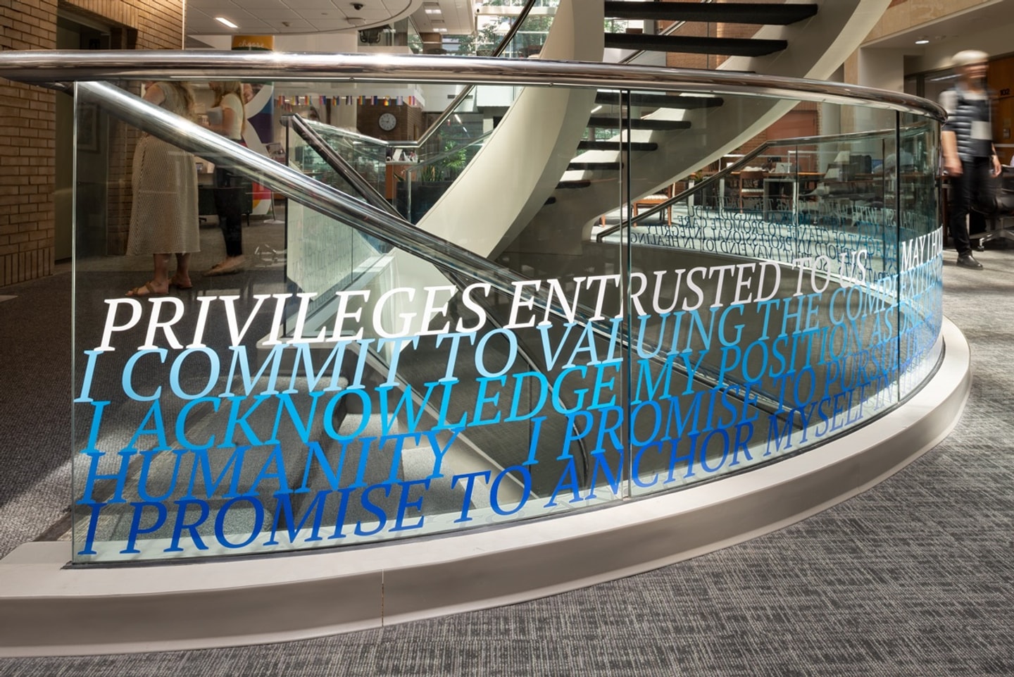 A staircase with glass sides and the hippocratic oath installed in blue vinyl