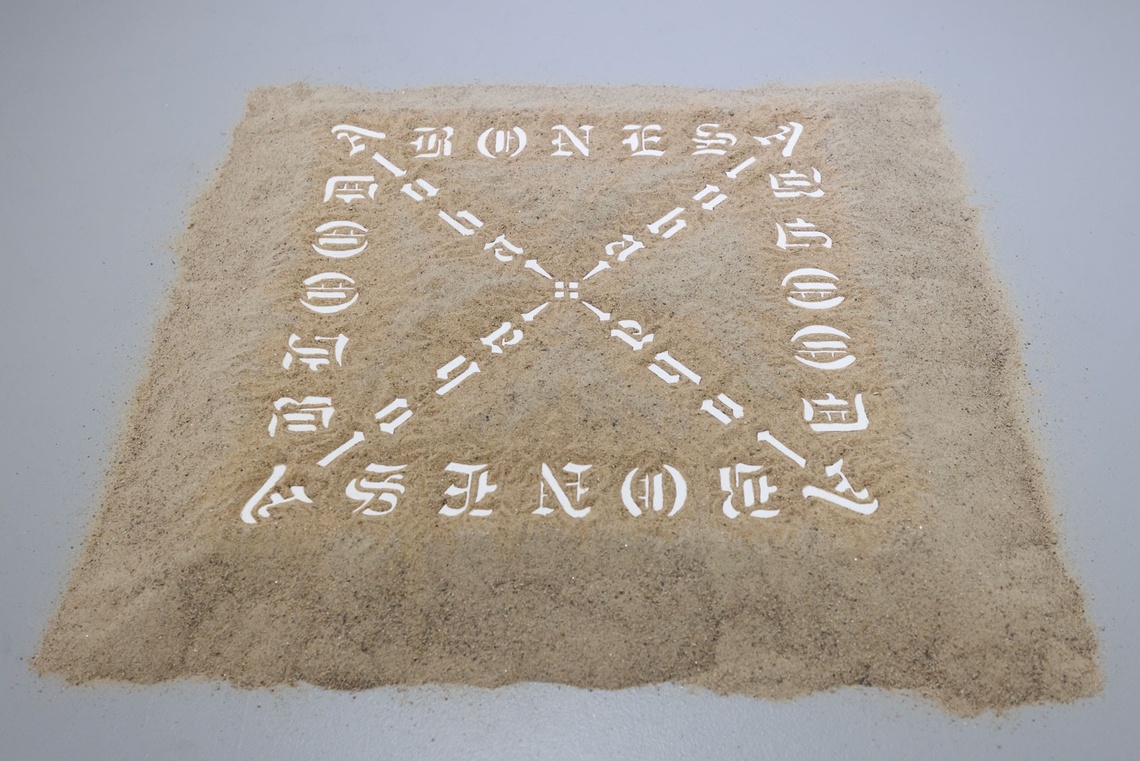 A square pile of sand inlaid with Gothic characters reading "blood" and "bloodless" in an X pattern