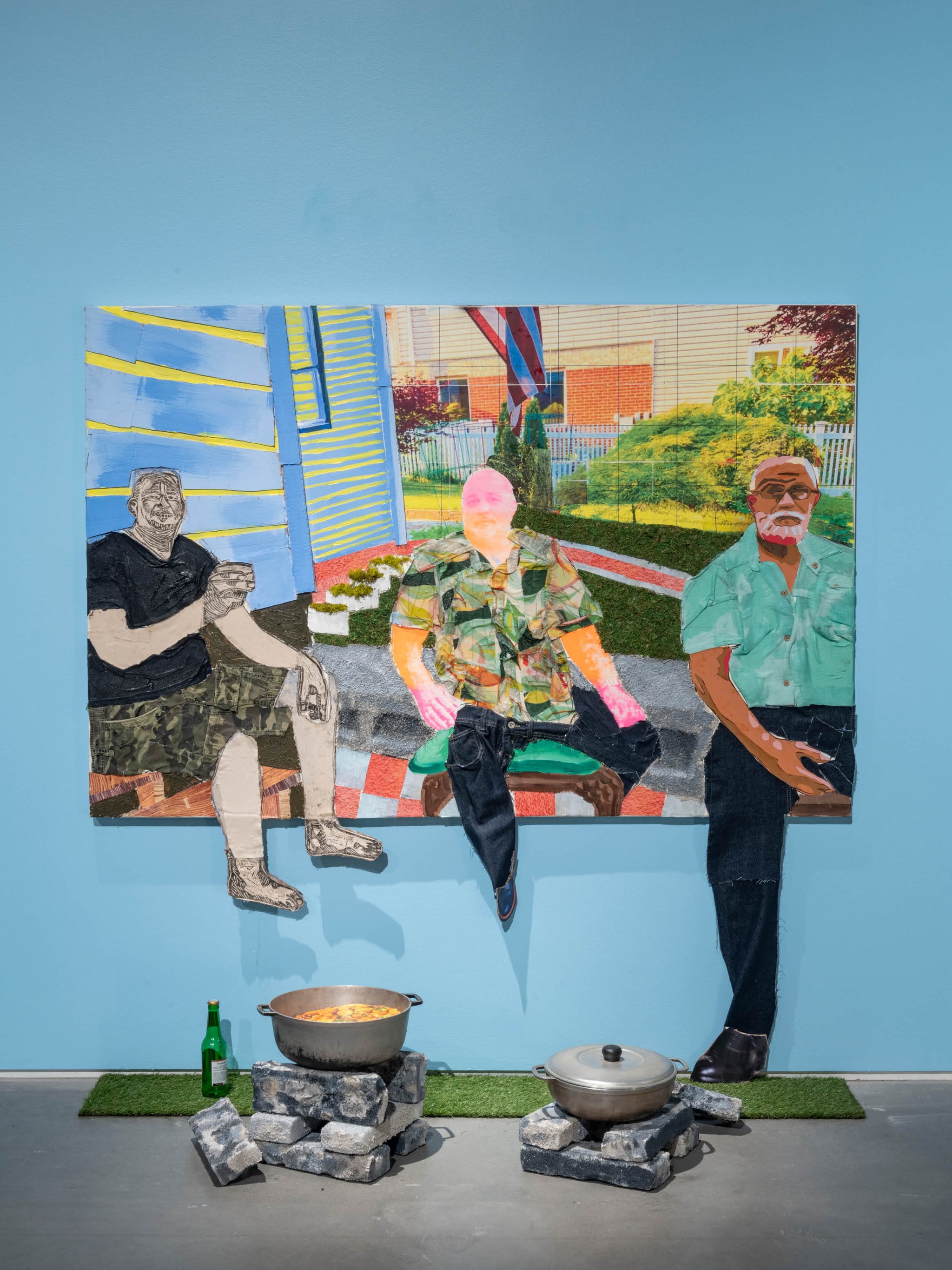 A mixed media painting depicting three Dominican men in a backyard in Yonkers, New York. The men each face the viewer, and elements on the painting extend down off the canvas onto the wall and floor. The men's legs all extend off the canvas. One of them touches the floor of the gallery, where a carpet of astroturf has been installed with metal pots on bricks representing the way the Dominican men are cooking food in the backyard.
