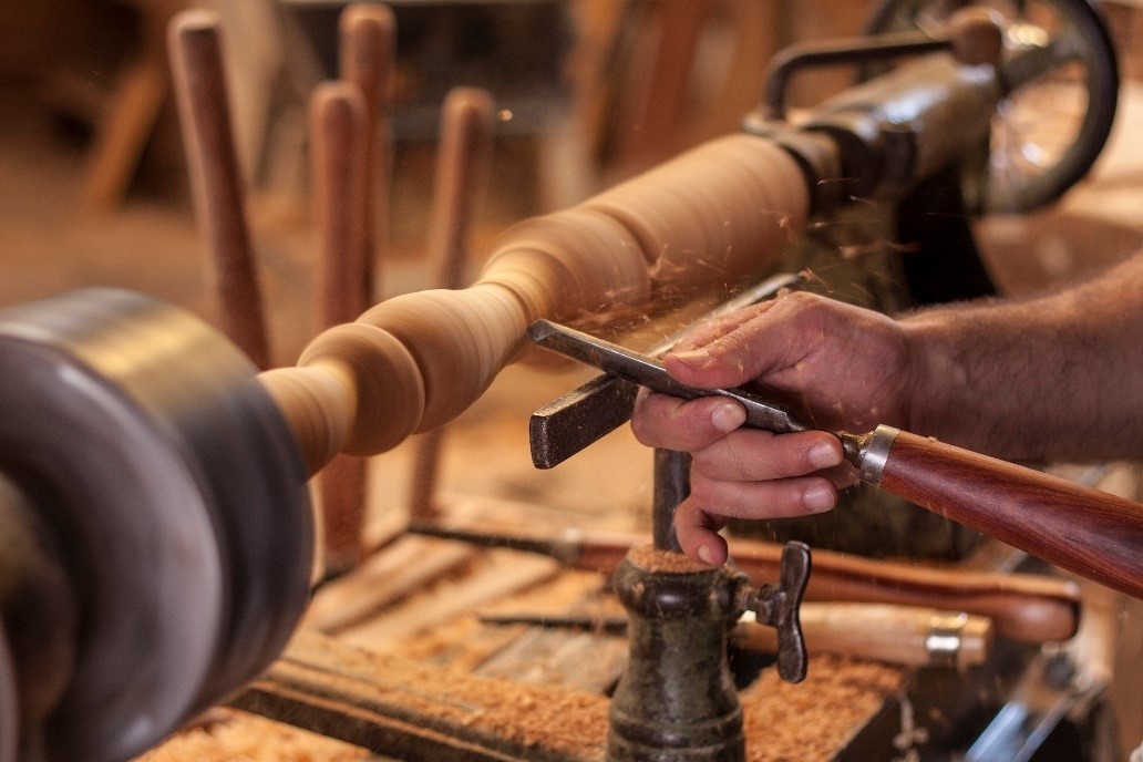 A hand holding a carving tool to a piece of wood turning on a lathe