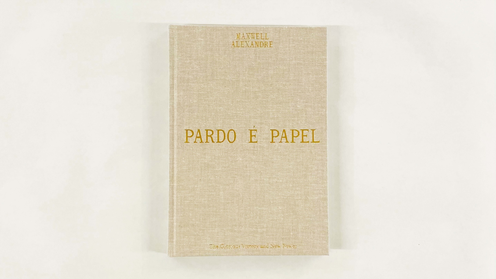 An exhibition catalogue with a hardback cover in tan-colored cloth. The cover reads Maxwell Alexandre, Pardo é Papel in gold letters. 