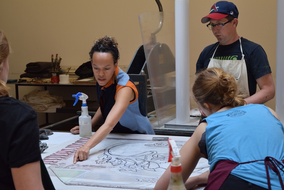 Paula points to the top right section of her print outline on the table while three other people look on