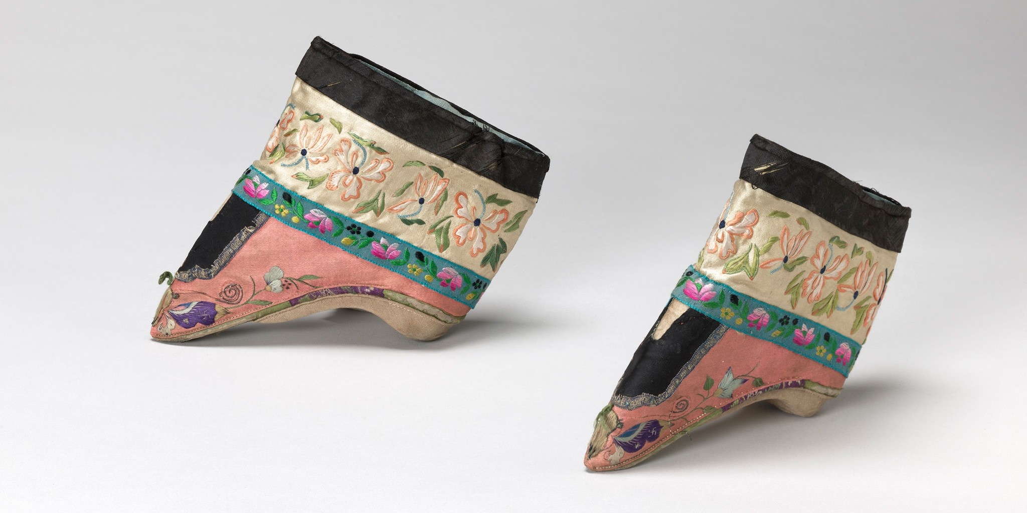 A pair of pink-and-cream-colored ankle-high shoes with embroidered flowers, leaves, and a purple-winged butterfly at the toe.