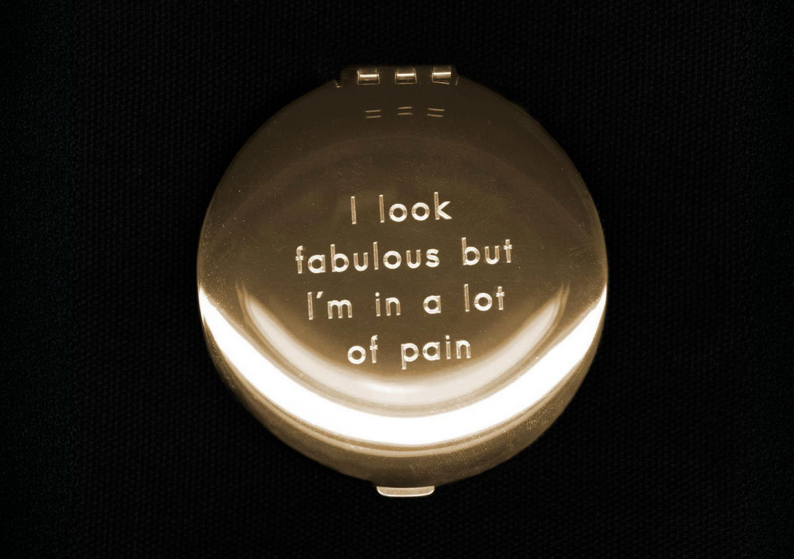 A gold compact mirror is etched to reveal the phrase, “I look fabulous but I’m in a lot of pain”