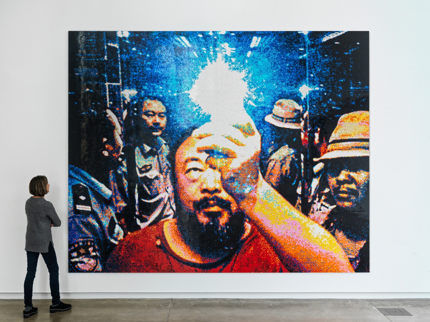 Installation view of person standing next to large Lego version of a photo of men in an elevator, one holding cell-phone camera to a mirror to take a selfie, the flash visible
