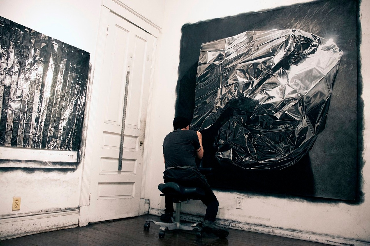 Man in studio working on large-scale black and white drawing of space blanket with another drawing hanging on wall next to him.