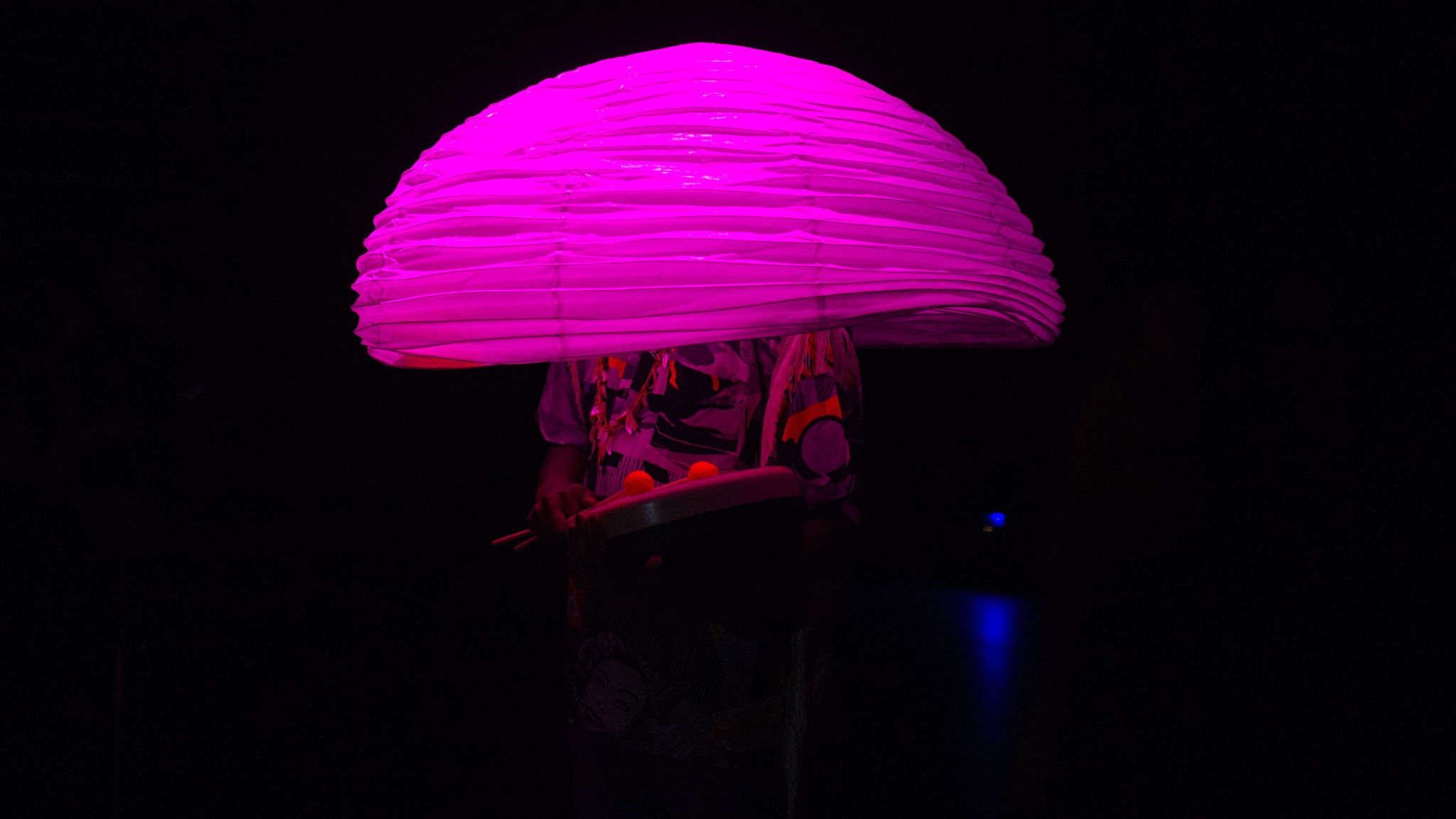 Person in pink light, under mushroom-like crepe object covering their upper body.
