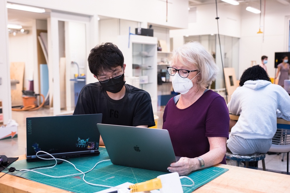 Instructor and student look at laptops at a worktable in a maker space.