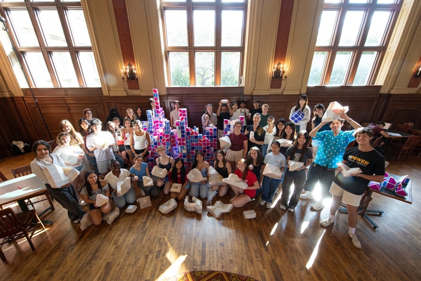 A group of students smile for the camera holding pieces of a 3D printed sculpture