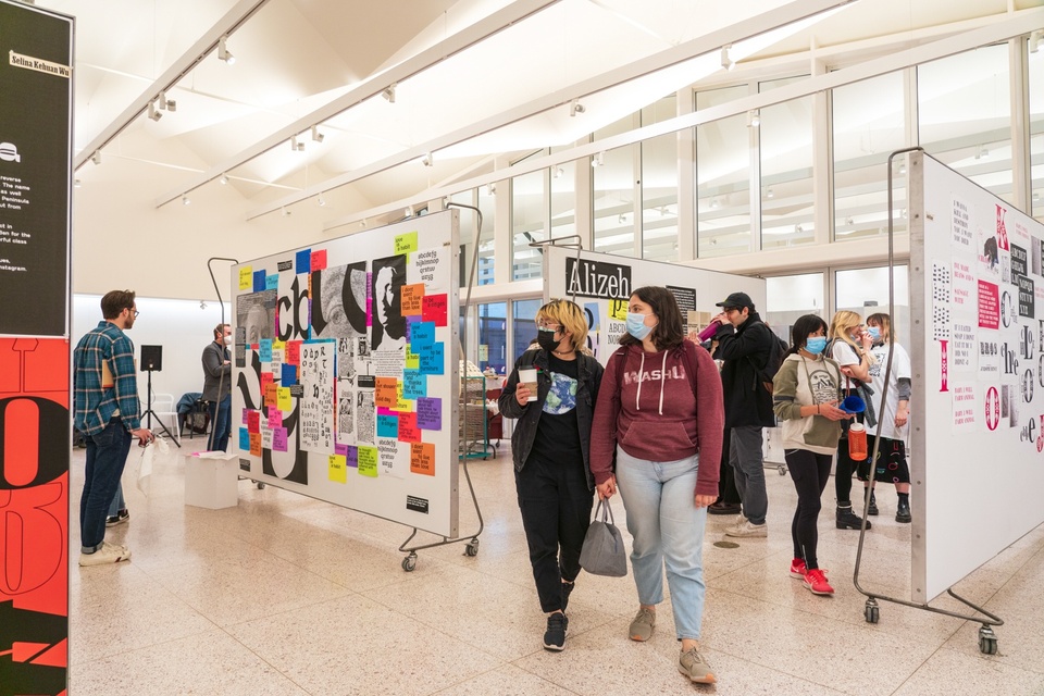 Wide shot of a gallery space full of people, displaying typographic prints.