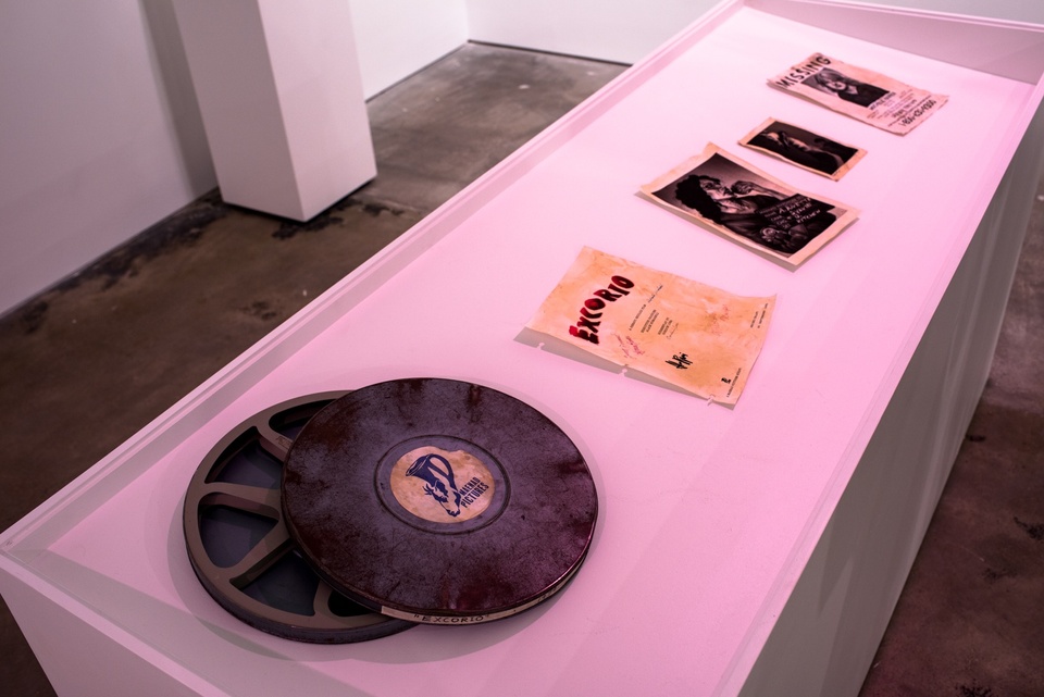 Display table with a film cannister, an aged flier titled "Excorio," two illustrated mugshots, and an illustrated Missing Person poster.