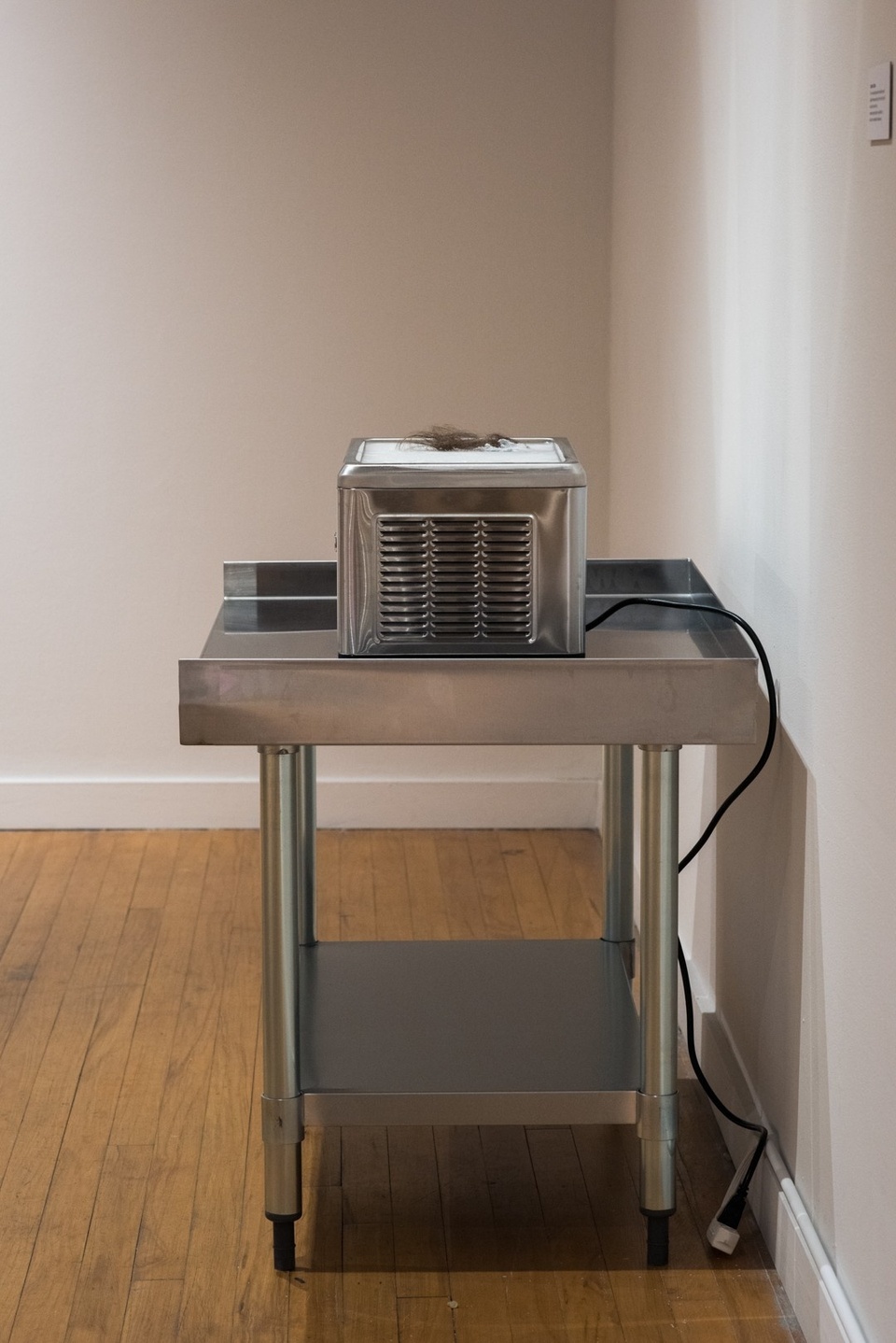 Metal utility cart with a boxy metal appliance sitting on top. A clump of dark hair is placed on the surface of the machine.