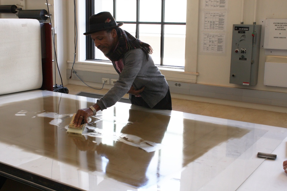 Artist drawing with a squeegee in the ink on monotype plate at the press