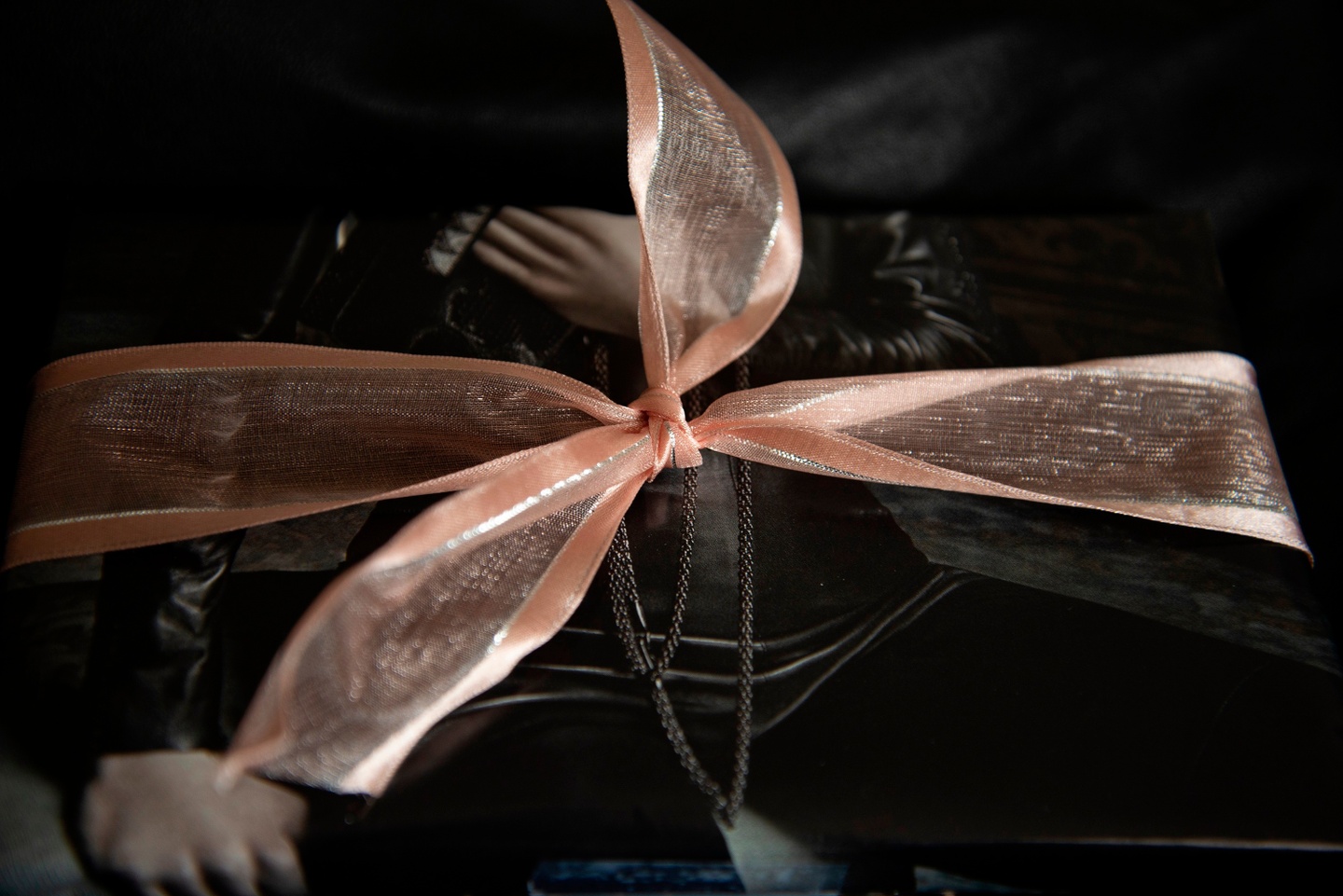 Closeup of a black gift box with a translucent peach ribbon on top