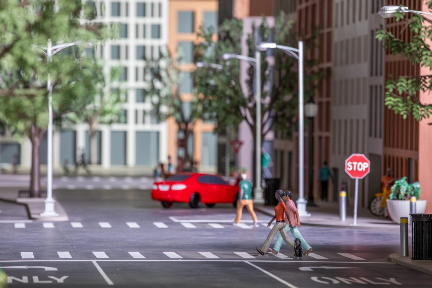 Image of mini city with model car and figurines on a street with buildings and trees in the background