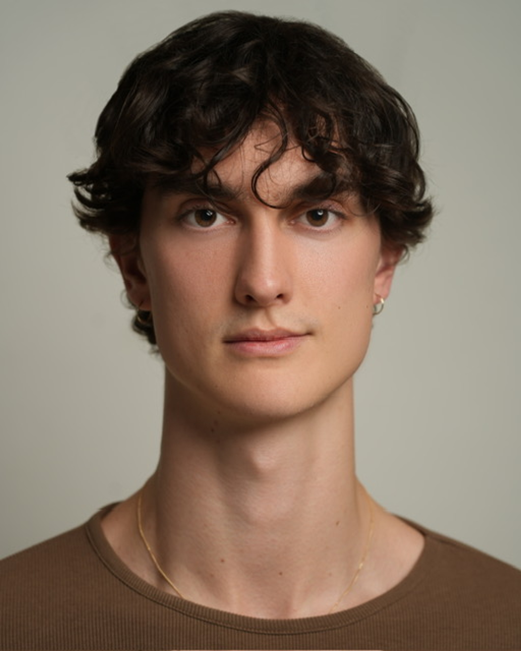 A headshot of dancer Thomas Hogan, a white man seen from the shoulders up. He has brown hair swept over his forehead and smiles slightly with one side of his mouth.
