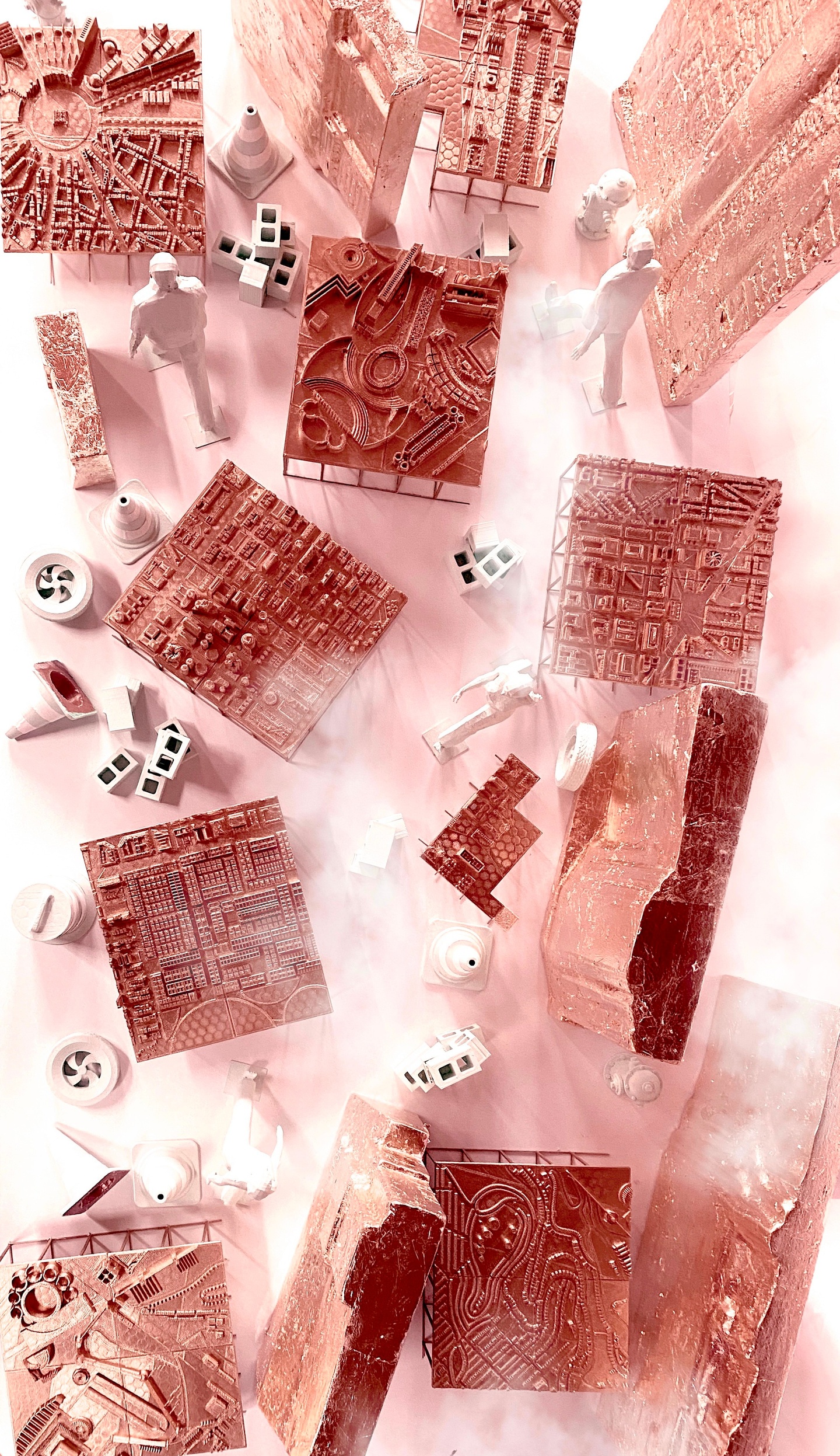 Overhead view of numerous wooden architectural models, with some concrete blocks and a couple of figures interspersed.