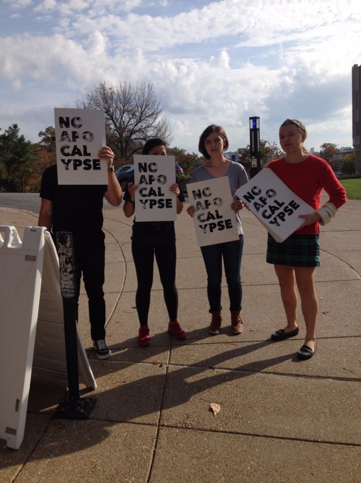 Four people standing in a row holding posters that say "No Apo Cal Ypse"