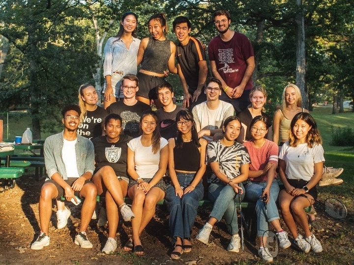 Large group of about 17 happy students seated/standing for a portrait outside.