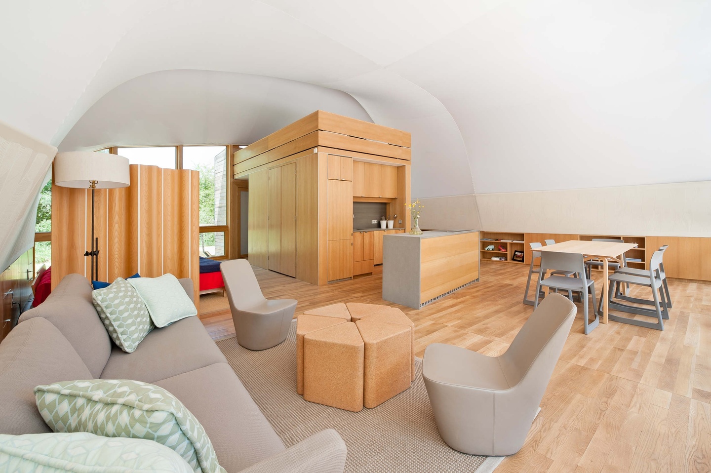 Interior of a house with curving, cavelike white walls and roof, bright wood floors and partitions, and modern beige furnishings.