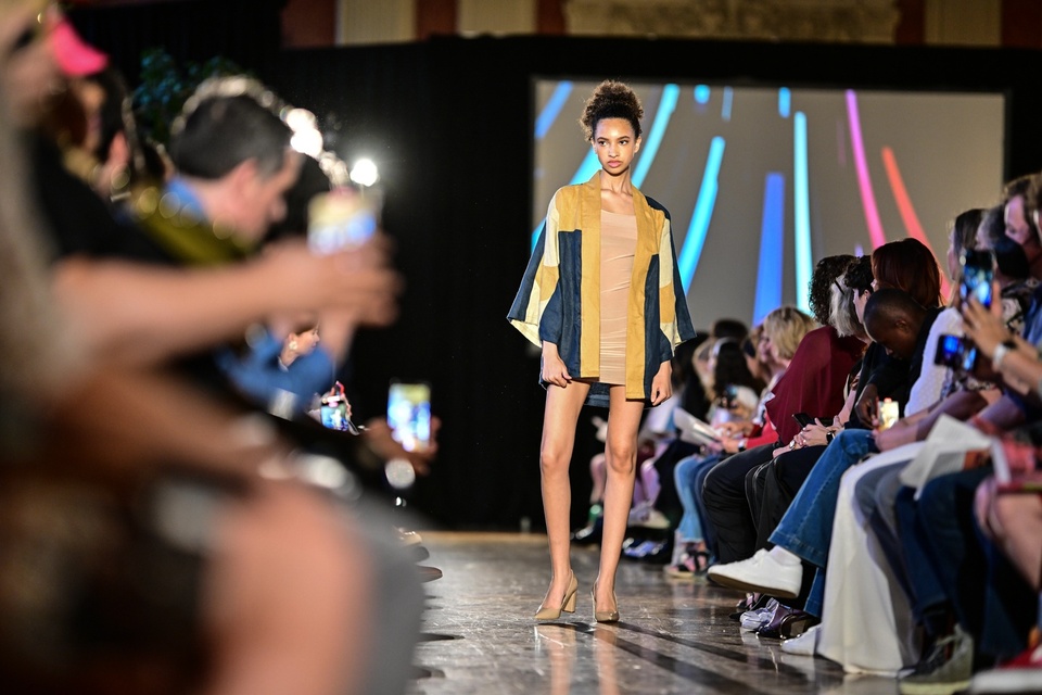 A model poses on the runway in a beige dress with a kimono-style green and yellow jacket