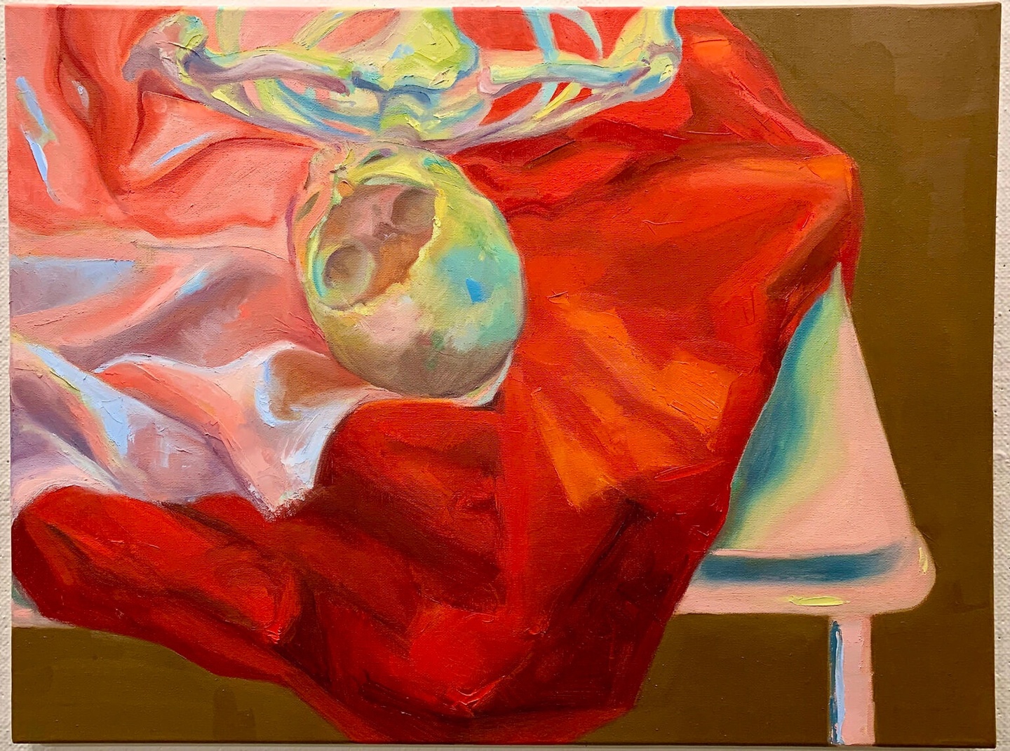 Oil on canvas painting of a skull atop a red/pink draped fabric on a table.