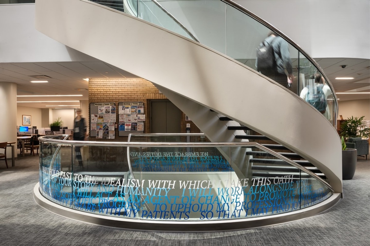 A curving staircase with glass sides and the hippocratic oath installed in blue vinyl