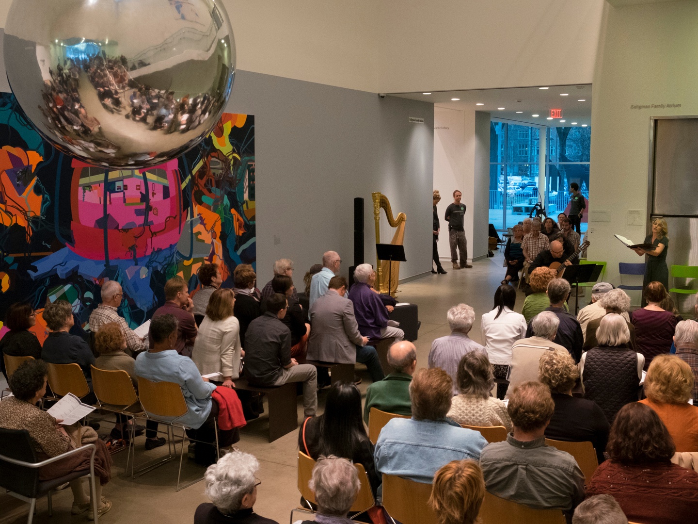 A guitarist and a singer performing in front of a seated audience in a museum