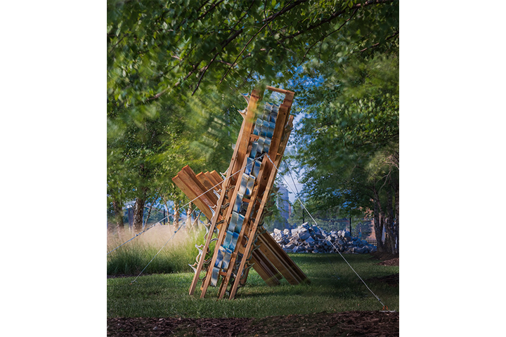 Wood and ceramic sculpture outdoors next to tree and native grasses