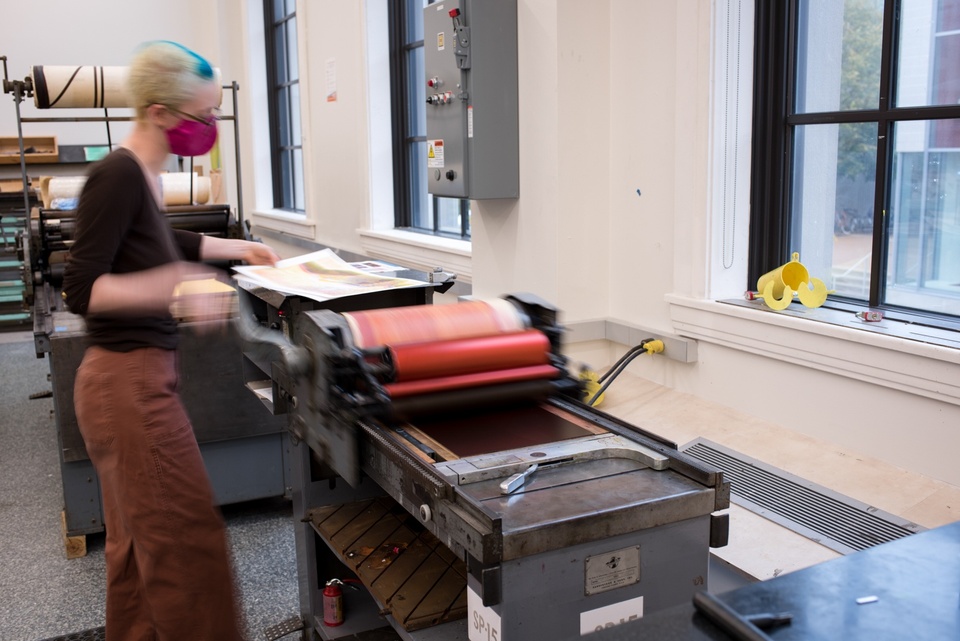 Student runs a print through a hand-cranked roller.