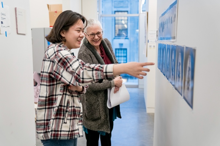 Two people look at some prints pinned to the outside wall of an artist's studio.